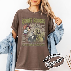 May include: Brown t-shirt with a graphic featuring the text "Oogie Boogie" and illustrations of characters. The shirt also has the text "Let's Roll the Dice!" and "I'm the Oogie Boogie Man!" The shirt is labeled "Comfort Colors Espresso".