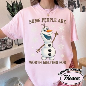 May include: A light pink t-shirt featuring a cartoon image of Olaf the snowman with the text "SOME PEOPLE ARE WORTH MELTING FOR". The shirt also has snowflake graphics.