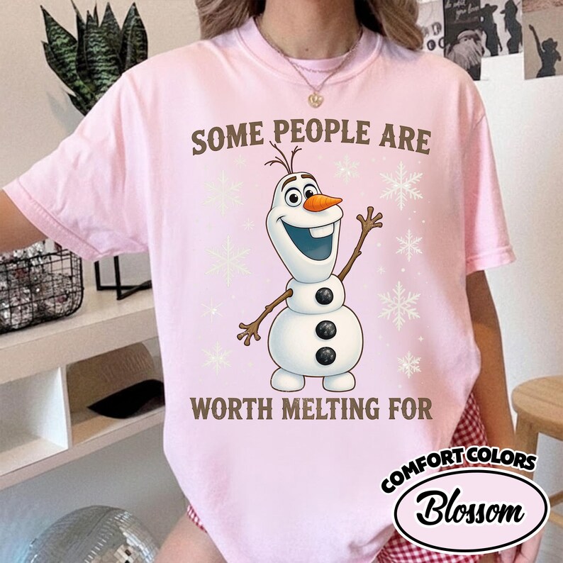 May include: A light pink t-shirt featuring a cartoon image of Olaf the snowman with the text "SOME PEOPLE ARE WORTH MELTING FOR". The shirt also has snowflake graphics.
