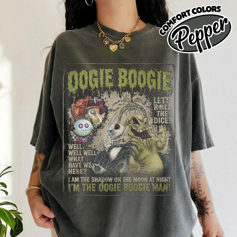 May include: Dark gray t-shirt featuring a graphic from "The Nightmare Before Christmas" with the text "Oogie Boogie." The design includes characters like Jack Skellington and Oogie Boogie. The shirt also has the text "Let's Roll the Dice!" and "I'm the Oogie Boogie Man!"