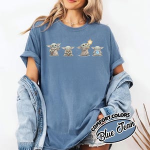 以下が含まれることがあります： グローグのキャラクターの4つのイラストが特徴のブルージーンズカラーのTシャツ。イラストは、さまざまなアイテムを持っているグローグを描いています。「COMFORT COLORS」と「Blue Jean」の文字がシャツの右下にプリントされています。