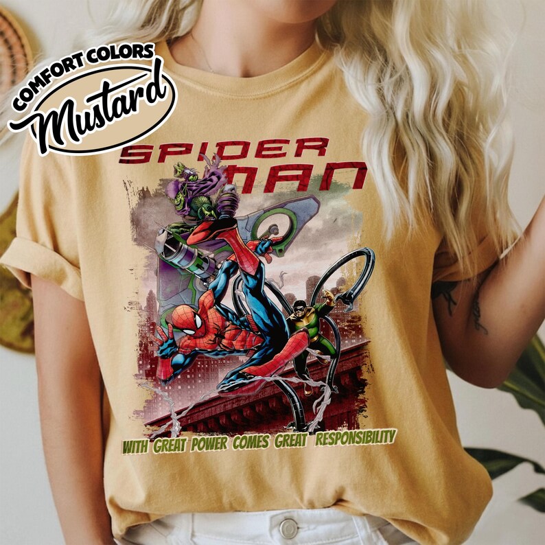 Op de afbeelding: Mosterdkleurig T-shirt met een Spider-Man-afbeelding. Het ontwerp toont Spider-Man in actie met schurken, de tekst "SPIDER-MAN" en de quote "WITH GREAT POWER COMES GREAT RESPONSIBILITY." Het shirt heeft opgerolde mouwen en een Comfort Colors label.