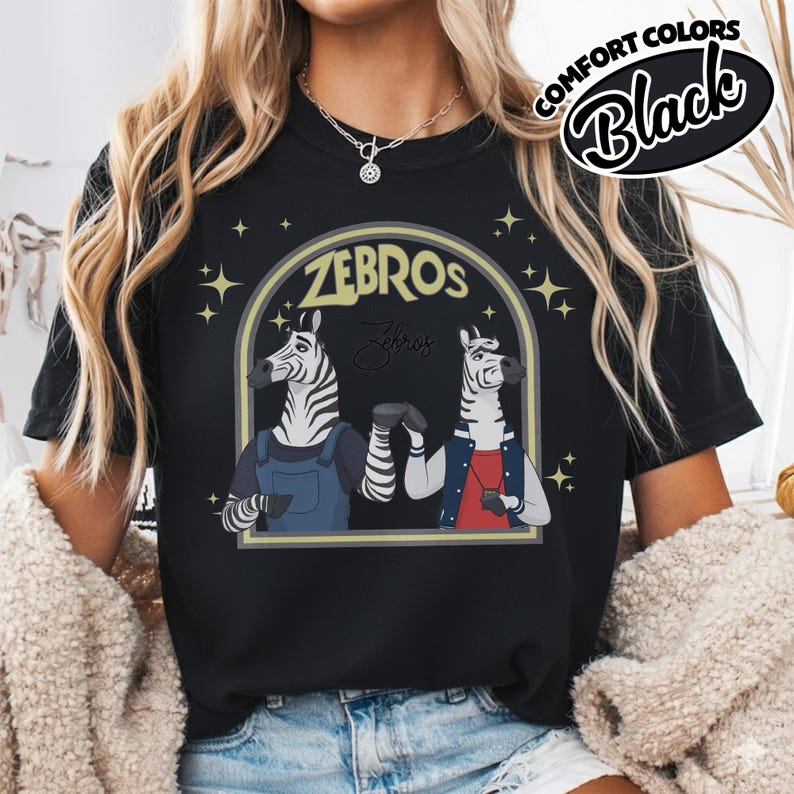 May include: Black t-shirt with a cartoon design of two zebras in an archway, with the word "ZEBROS" above them. The zebras wear outfits, and the text "Comfort Colors Black" is in a circle.