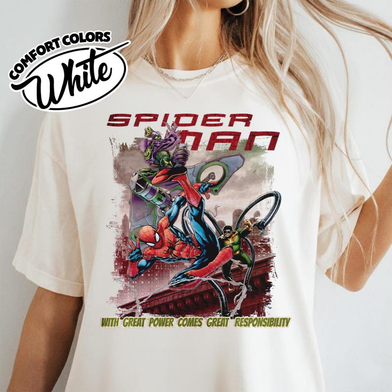 Op de afbeelding: Wit T-shirt met een Spider-Man-afbeelding. Het ontwerp bevat de tekst "Spider-Man" in het rood en de zin "Met grote macht komt grote verantwoordelijkheid." De afbeelding toont Spider-Man in actie met andere personages.