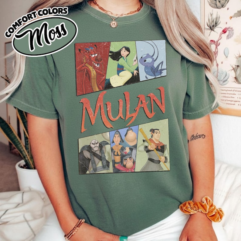 Puede incluir: Una camiseta verde musgo con un dise&ntilde;o gr&aacute;fico de la pel&iacute;cula de animaci&oacute;n Mulan. El dise&ntilde;o incluye el t&iacute;tulo de la pel&iacute;cula e ilustraciones de personajes. La camiseta tiene mangas cortas y cuello redondo.