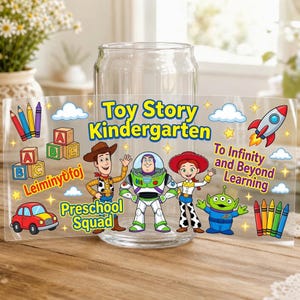 May include: A clear glass tumbler featuring a colorful Toy Story theme with characters Woody, Buzz Lightyear, Jessie, and an alien. The design includes text reading Toy Story Kindergarten, Preschool Squad, and To Infinity and Beyond Learning.