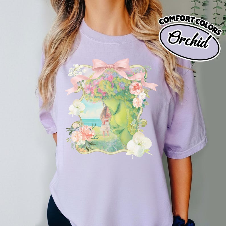 K&ouml;nnte beinhalten: Ein helllila T-Shirt mit einem floralen Aufdruck. Die Grafik zeigt ein gr&uuml;nes Gesicht mit Blumenkrone, eine rosa Schleife und eine Strandszene. Der Text "COMFORT COLORS Orchid" befindet sich in einem wei&szlig;en Oval.