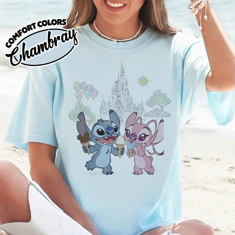 Puede incluir: Camiseta azul claro con una ilustraci&oacute;n de Stitch y Angel, cada uno sosteniendo un cono de helado frente a un castillo. La camiseta tiene las palabras "COMFORT COLORS" y "Chambray" impresas en la parte superior izquierda.