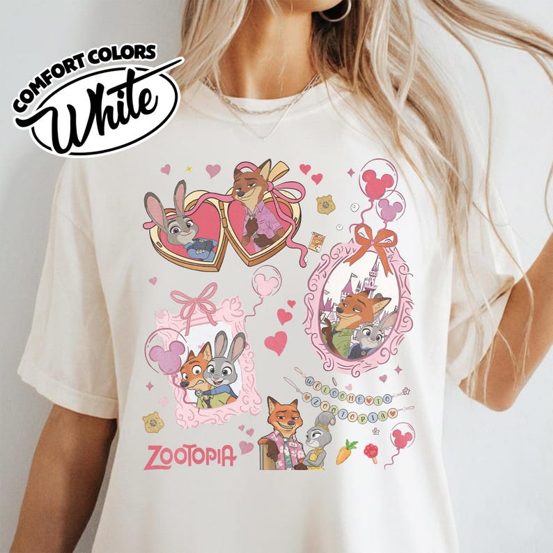 May include: A white t-shirt featuring a graphic print of Zootopia characters Judy Hopps and Nick Wilde. The design includes heart-shaped frames, a castle-themed border, pink balloons, and the text Zootopia, with a Comfort Colors White logo in the corner.