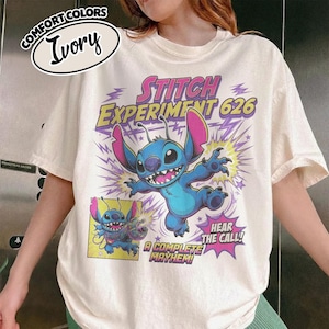 Może przedstawiać: Koszulka w kolorze kości słoniowej z grafiką niebieskiej postaci Stitcha z Experiment 626. Projekt zawiera tekst STITCH EXPERIMENT 626, HEAR THE CALL oraz A COMPLETE MAYHEM, wraz z mniejszym wstawionym obrazkiem postaci.