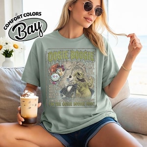 May include: A light green t-shirt featuring a graphic from "The Nightmare Before Christmas" with the text "Oogie Boogie". The shirt has the words "Comfort Colors" and "Bay" printed on the top left.