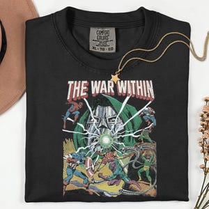 May include: Black t-shirt with a comic book graphic featuring the text "THE WAR WITHIN" and various superhero characters. A gold star pendant necklace is draped over the shirt. The shirt has a Comfort Colors tag, size XL-TG-EG.