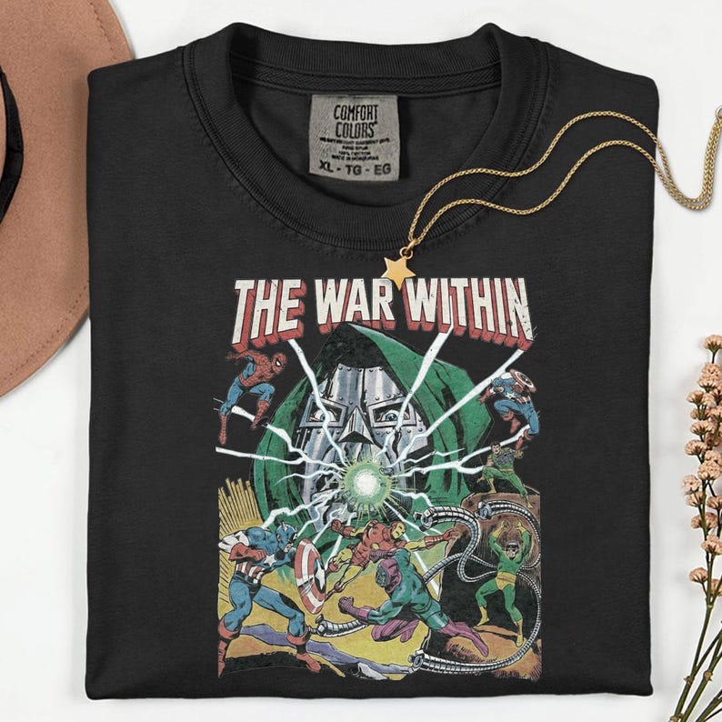 May include: Black t-shirt with a comic book graphic featuring the text "THE WAR WITHIN" and various superhero characters. A gold star pendant necklace is draped over the shirt. The shirt has a Comfort Colors tag, size XL-TG-EG.