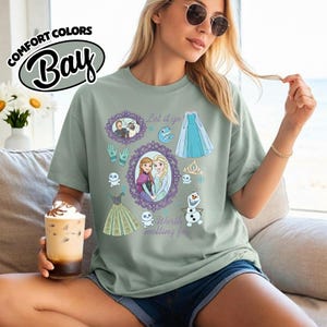 Op de afbeelding: Saliegroen T-shirt met een afbeelding van personages en elementen uit de film Frozen. Het ontwerp bevat illustraties van Anna en Elsa, een jurk en de tekst "Let it go" en "Worth melting for."