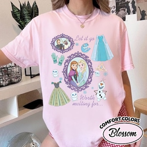 Op de afbeelding: Een lichtroze Comfort Colors T-shirt met een Frozen-thema. Het ontwerp bevat illustraties van personages en elementen uit de film, samen met de zinnen "Let it go" en "Worth melting for..."