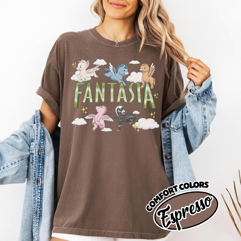 May include: A brown t-shirt with the word "Fantasia" in green, and cartoon pegasus characters in different colours. The shirt has a vintage look with the words "Comfort Colors" and "Espresso" in a circular design.