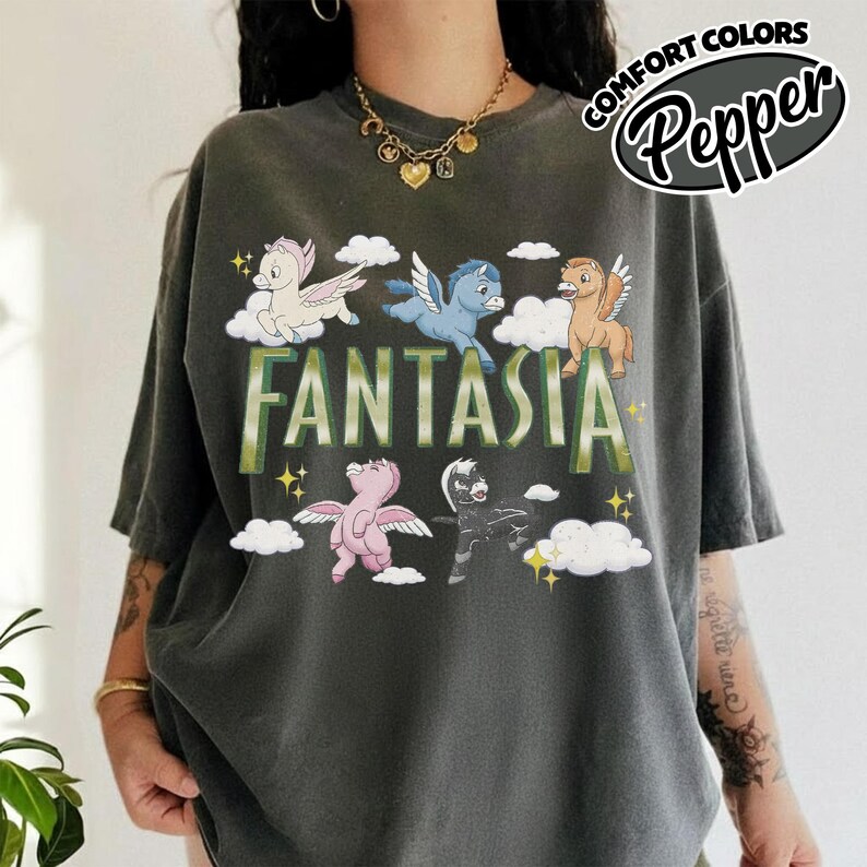 May include: Dark grey t-shirt featuring the word "FANTASIA" in green, with cartoon pegasus characters. The shirt also has the words "COMFORT COLORS" and "Pepper" in a circular design.