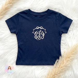 Op de afbeelding: Marineblauw T-shirt met een wit monogram ontwerp. Het shirt heeft korte mouwen en een ronde hals. Het monogram toont de letters "GFJ" in een decoratief schrift, omringd door een strik.