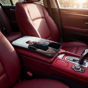 May include: A rectangular car armrest cover with a printed image of a couple. The cover is placed on a red leather car armrest. The car interior features red leather seats and a console with a gear shift.