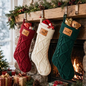 May include: Three cable-knit Christmas stockings in red, cream, and dark green, each featuring a leather patch with the names Rocky, Xixi, and Jacky engraved. The stockings are hung from metal hooks and contain small gifts and a teddy bear.