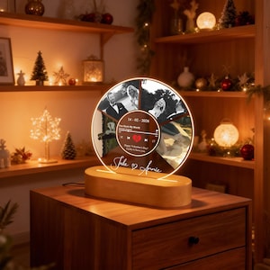 May include: A personalized illuminated photo display featuring a circular design with multiple photos and text. The display sits on a wooden base and includes the names "Jake & Annie". The photos are in black and white.
