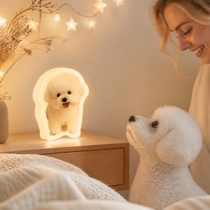 May include: A custom-shaped LED lamp featuring a printed image of a white Bichon Frise dog. The lamp emits a warm, soft glow and is contoured to the silhouette of the dog, displaying the animal with a small circular tag around its neck.