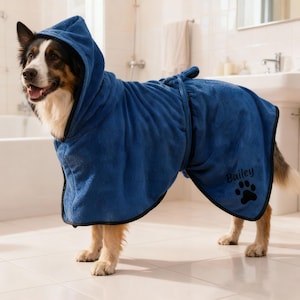 May include: A blue dog robe with a hood and black trim, worn by a dog in a bathroom. The robe is personalised with the name "Bailey" and a paw print. The dog is a mix of black, white, and brown.