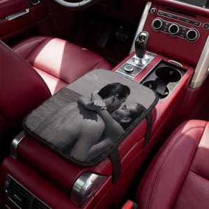 May include: A car console cover with a black and white image of a couple kissing. The cover is rectangular and sits on the console of a red car interior. The car interior includes red leather seats and a gear stick.