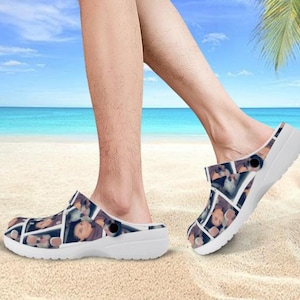 Puede incluir: Zuecos blancos con un diseño de collage de fotos. Los zuecos tienen una suela blanca y un botón negro en el lateral. El collage de fotos presenta una variedad de imágenes. Los zuecos se llevan en una playa arenosa.