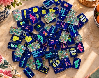 May include: A collection of rectangular Mahjong tiles featuring a deep blue base with embedded multicolored glitter. The tiles display various bright yellow, pink, and green symbols, including numbers, dragons, flowers, and the word JOKER.