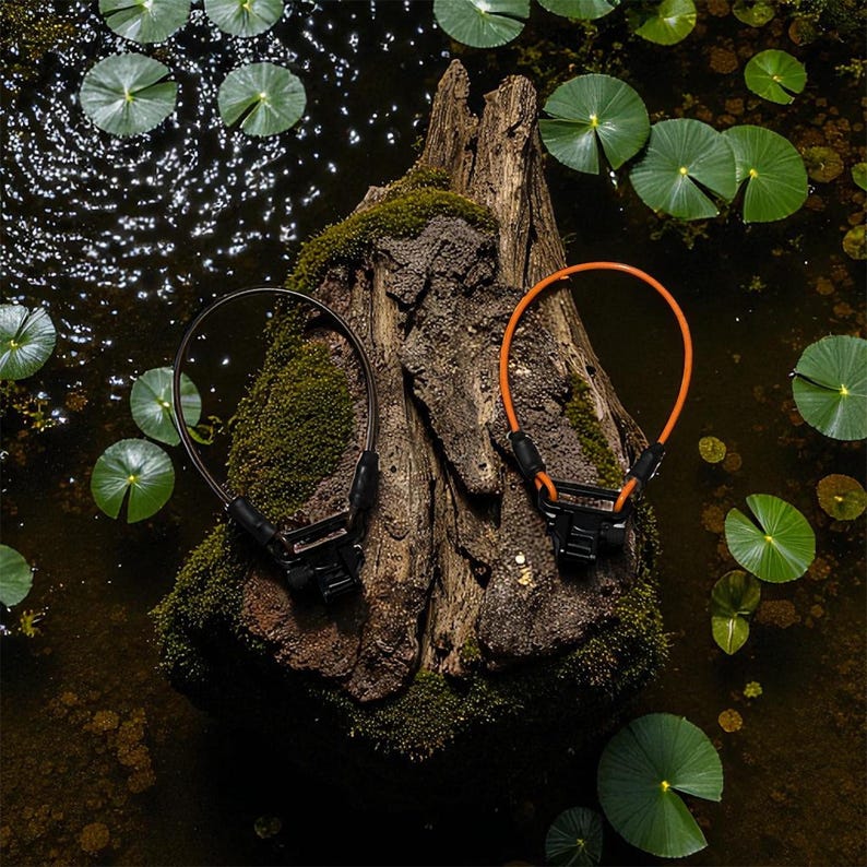 Pode incluir: Duas fechaduras de cabo de bicicleta, uma castanha e outra laranja, repousam sobre um tronco de &aacute;rvore coberto de musgo em um lago com nen&uacute;fares. As fechaduras t&ecirc;m mecanismos de travamento pretos.
