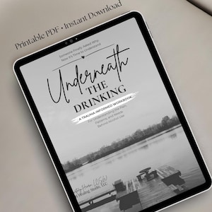 May include: A digital tablet displaying a workbook cover titled Underneath The Drinking, A Trauma-Informed Workbook For Understanding the Pain, Patterns, and Needs Behind Alcohol Use, featuring a black and white lake scene with a wooden dock.