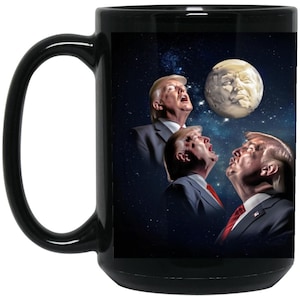 May include: A black coffee mug with a white image of three men with their mouths open, looking up at a moon-like object in the sky. The background is a dark blue with stars.