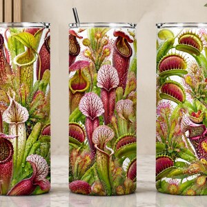 May include: A set of three stainless steel tumblers with a vibrant botanical design featuring carnivorous plants. The design includes pitcher plants, Venus flytraps, and other exotic flora in shades of red, green, and white. Each tumbler has a silver straw.