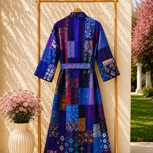May include: A long-sleeved robe featuring a patchwork design in various shades of blue, purple, and violet. The garment includes a matching tie belt at the waist and is constructed from multiple rectangular fabric panels with visible stitching.