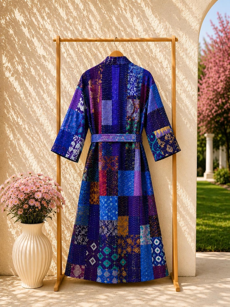 May include: A long-sleeved robe featuring a patchwork design in various shades of blue, purple, and violet. The garment includes a matching tie belt at the waist and is constructed from multiple rectangular fabric panels with visible stitching.