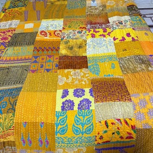 May include: A patchwork quilt featuring a vibrant array of yellow, gold, and mustard fabric panels. The textile displays diverse patterns including floral motifs, geometric shapes, and paisley prints, all joined together with visible running stitch details.