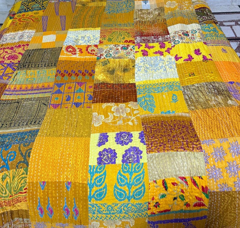 May include: A patchwork quilt featuring a vibrant array of yellow, gold, and mustard fabric panels. The textile displays diverse patterns including floral motifs, geometric shapes, and paisley prints, all joined together with visible running stitch details.