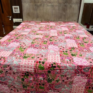 May include: A rectangular quilt featuring a vibrant pink base colour with a repeating patchwork pattern. The design incorporates various floral motifs in shades of green, white, and dark pink, alongside intricate geometric and lattice-style prints.