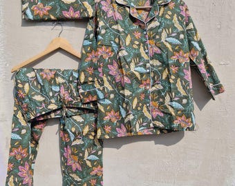 May include: A green floral pajama set with a matching storage pouch. The set includes a button-down shirt, trousers, and a pouch, all adorned with pink, yellow, and blue floral patterns. White trim accents the collar, cuffs, and pocket.