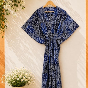 May include: A floor-length kaftan dress in a deep navy blue fabric featuring a white intricate paisley and bandana-style pattern. The garment has wide, flowing sleeves, a V-neckline, and a drawstring waist tie that gathers the fabric at the center.