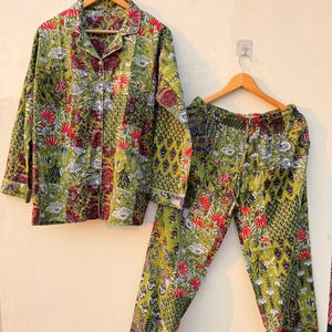 May include: A two-piece pajama set featuring a button-down shirt and matching pants. The set is adorned with a floral pattern in shades of green, red, and white. The shirt has a collared neckline and long sleeves. The pants have a relaxed fit.