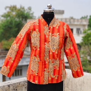 May include: An orange jacket with a tiger print. The jacket has a mandarin collar, long sleeves, and two front pockets. The tiger pattern is in black and tan, set against vertical red stripes.