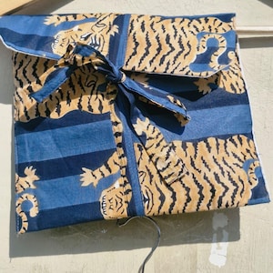 May include: A folded blue fabric item with a tiger print in tan and black, tied with a blue ribbon. The fabric has blue stripes and a white border. The item is hanging on a wooden hanger.