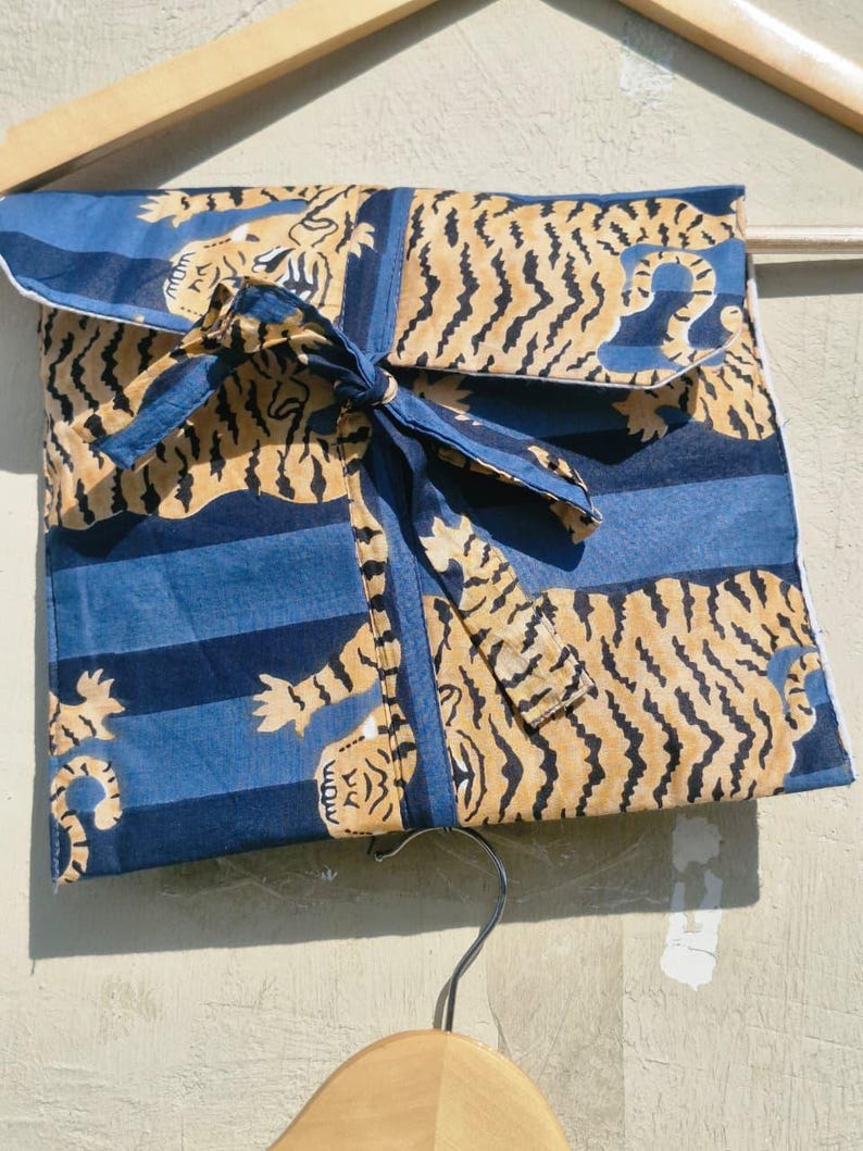 May include: A folded blue fabric item with a tiger print in tan and black, tied with a blue ribbon. The fabric has blue stripes and a white border. The item is hanging on a wooden hanger.
