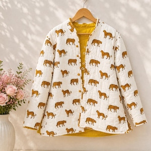 May include: A quilted jacket featuring a white exterior with a repeating pattern of brown leopards and a solid mustard yellow interior. The jacket has long sleeves, a mandarin collar, and a front closure with small fabric-covered buttons.