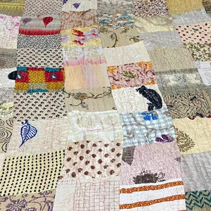 May include: A patchwork quilt constructed from rectangular fabric panels featuring a variety of patterns including floral, geometric, and abstract prints in shades of beige, white, red, blue, and black, with visible running stitch quilting details.