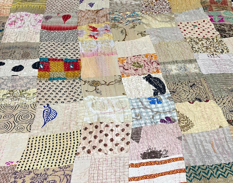 May include: A patchwork quilt constructed from rectangular fabric panels featuring a variety of patterns including floral, geometric, and abstract prints in shades of beige, white, red, blue, and black, with visible running stitch quilting details.