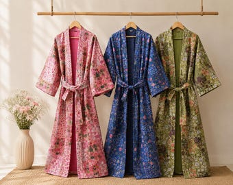 May include: Three long-sleeved robes with matching tie belts, each featuring a distinct floral pattern in shades of pink, blue, and green. The robes have an open front design, wide sleeves, and a quilted texture, hanging side by side on wooden hangers.