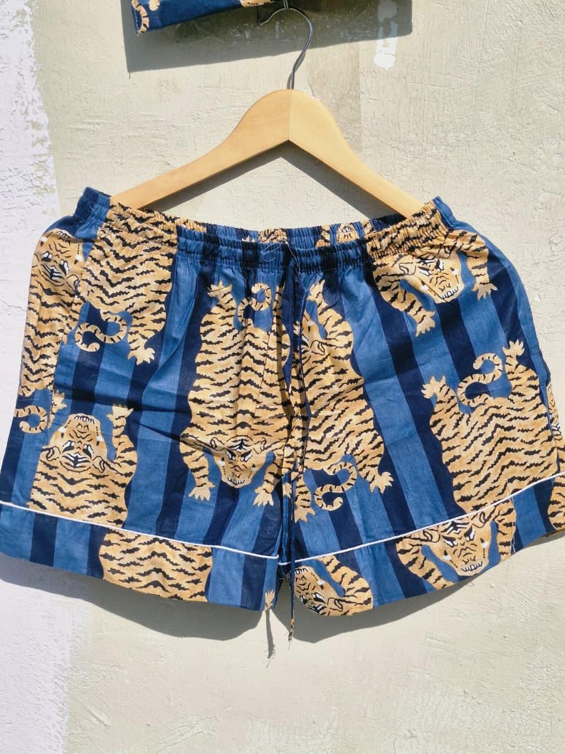 May include: Blue and tan tiger print shorts with a drawstring waist and white trim. The shorts are hanging on a wooden hanger. The fabric features a repeating pattern of tigers and blue vertical stripes.